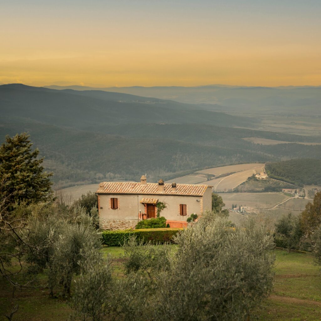 pexels-photo-6771585-6771585 A serene view of a rustic house surrounded by rolling hills in the Tuscan countryside at sunset.